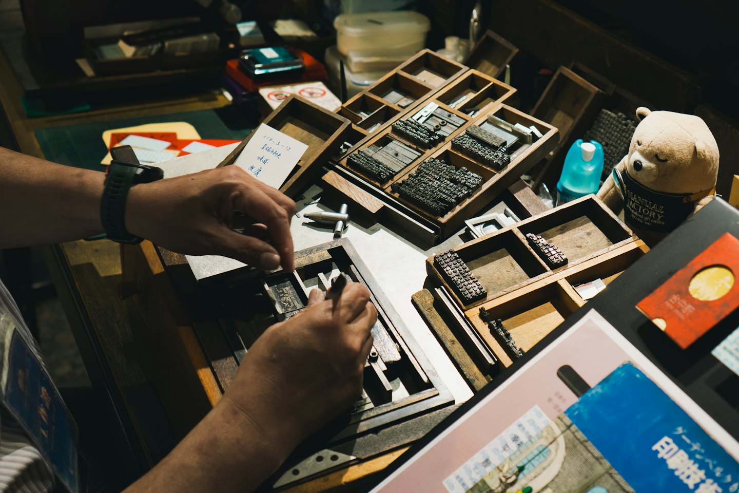 Hands arranging metal letterpress type in a composing stick.